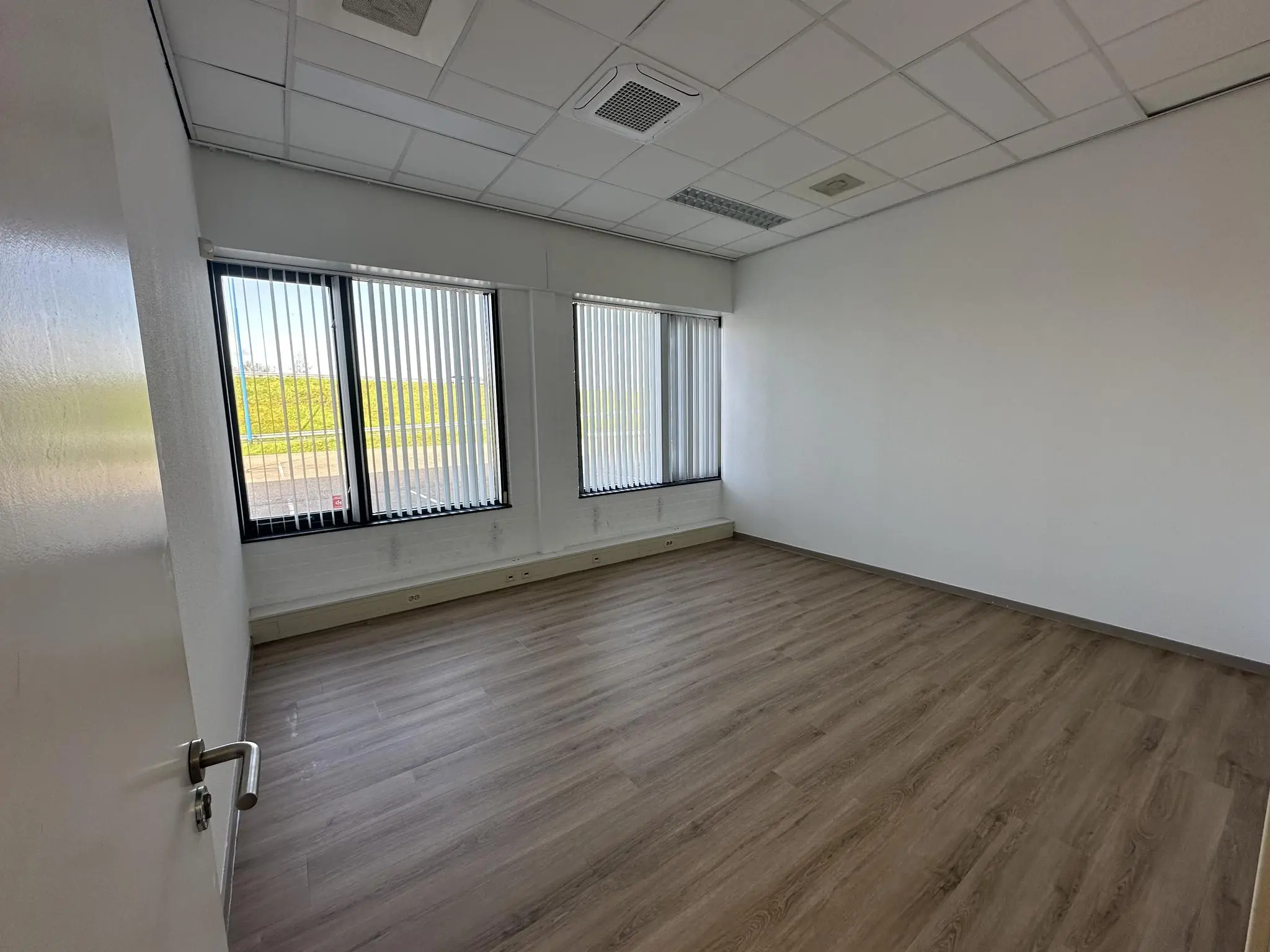 Leeg kantoorpand aan de Van der Hagenstraat met laminaatvloer en grote ramen met verticale lamellen.